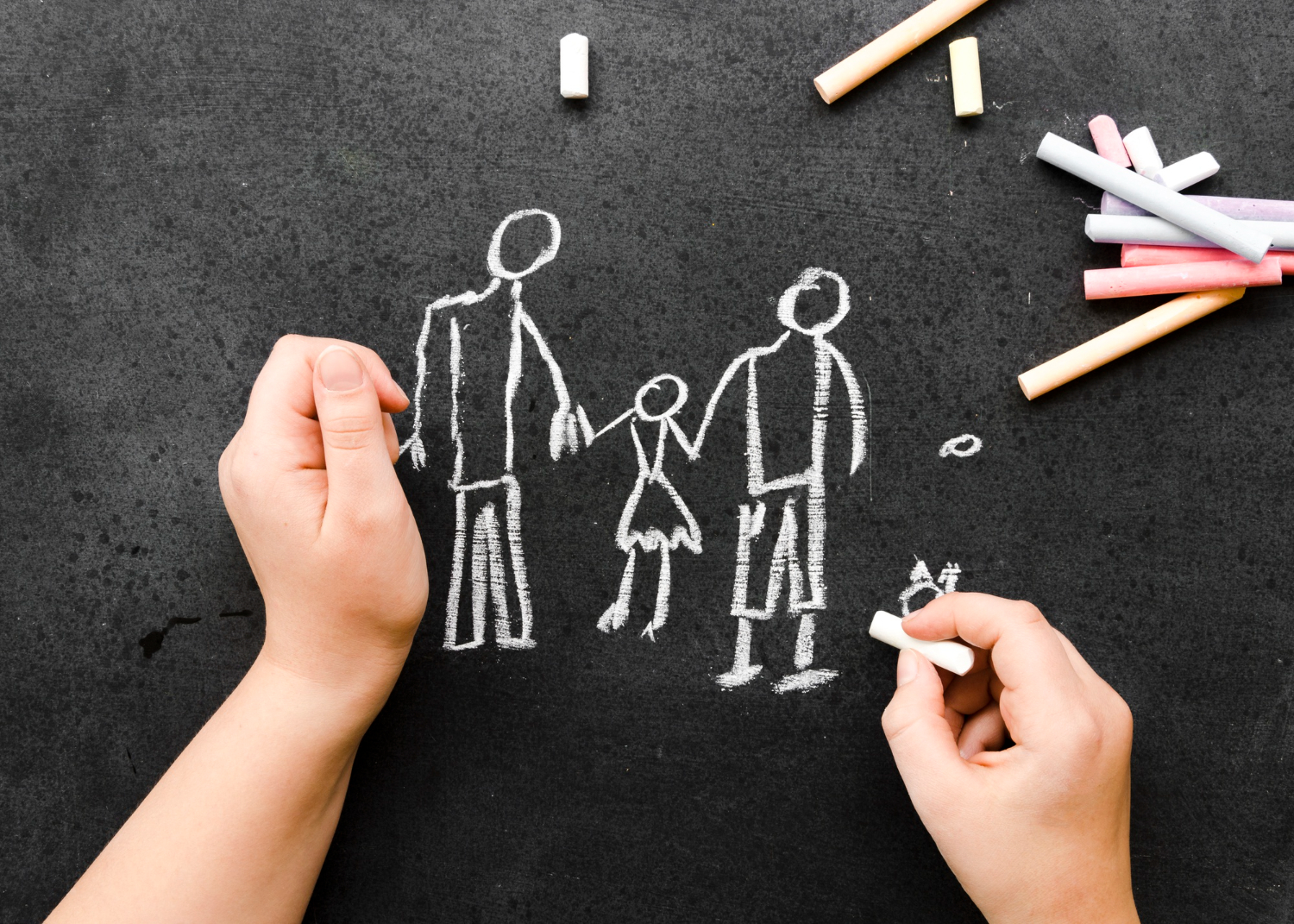 Blackboard image with chalk drawings of two parent-style figures holding the hands of a child girl