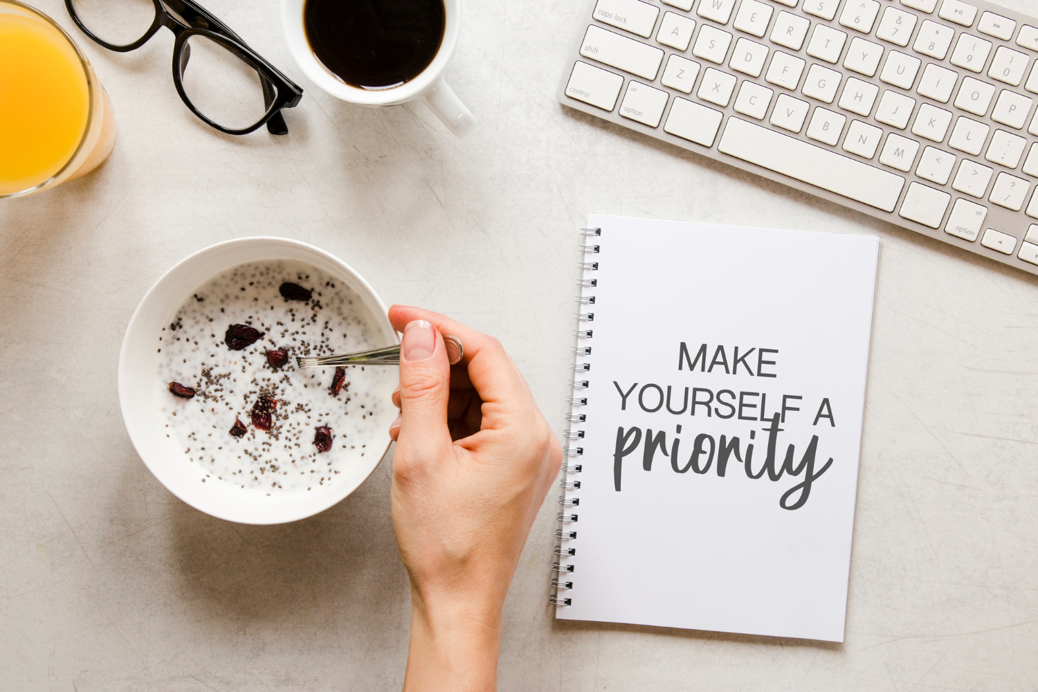 Desktop background with keyboard, oatmeal, coffee, glasses and card that says "make yourself a priority"